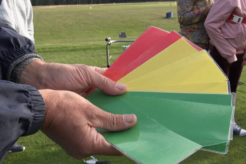 Närbild på två händer som håller upp sex stora plastkort - två röda, tre gula och tre gröna.