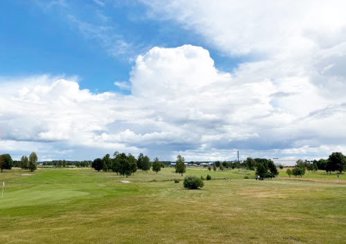 Vy över en golfbana. I bakgrunden blå himmel och vita sommarmoln
