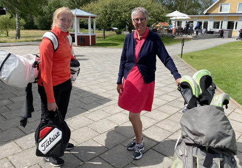Två kvinnor med varsin golfbag står framför ett klubbhus. En yngre och en äldre.
