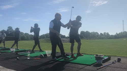 Driving range där golftränare undervisar fyra personer i golf och svingteknik. 
