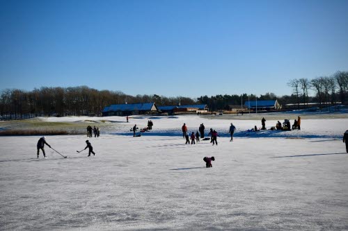 En golfanläggning i strålande sol, täckt med snö och is. Människor spelar hockey, grillar korv och åker skidorl. 
