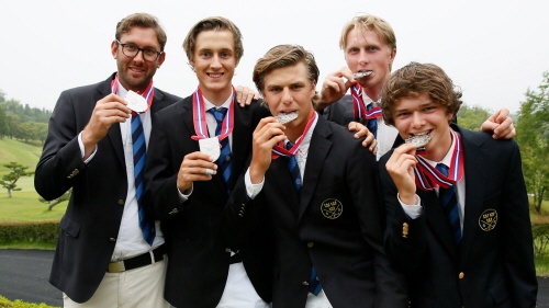 Bild på fem killar i mörkblå kavajer varav tre biter i sina silvermedaljer och de andra två håller upp sina.