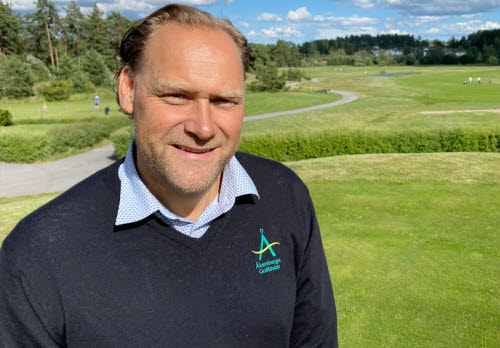 Man i medelåldern med svart v-ringad tröja med Åkersberga GK:s logotyp. Står på en golfbana en fin sommardag. 