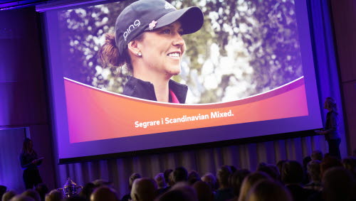 Publik tittar upp på en skärm där man ser en leende Linn Grant i golfkeps, med texten Segrare i Scandinavian Mixed.