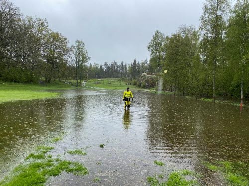 En översvämmad fairway på en golfbana. En person i arbetskläder vadar genom vattnet. 