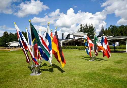 I bilden ser man två grupper av vajande flaggor  från olika nationer som är fästa i marken. 
