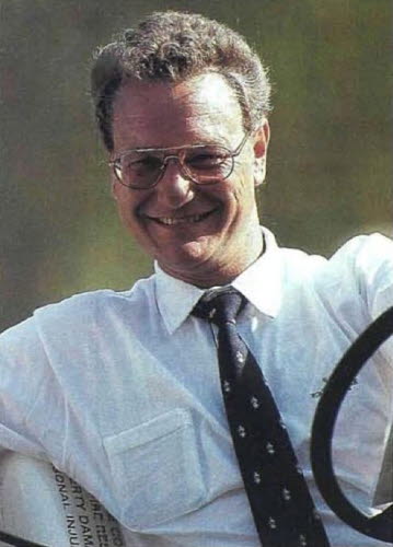 Äldre, lite grynig bild på leende man i 40-årsåldern i glasögon, vit skjorta och slips, sittande i en golfbil.  