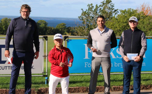 Fyra golfspelare i yngre medelåldern står framför en folksamskylt på en golfbana. Två håller i pokaler. En är kortväxt, en är lång, två medellängd. I bakgrunden syns havet.